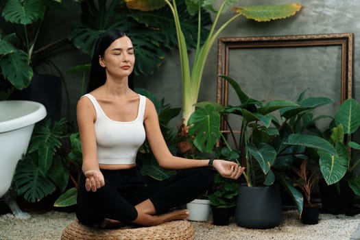 Young woman doing morning yoga and meditation in natural garden with plant leaf, enjoying the solitude and practicing meditative poses. Mindfulness activity and healthy mind lifestyle. Blithe