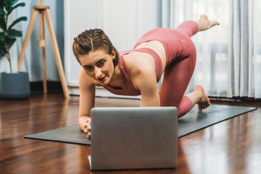 Flexible and dexterity woman in sportswear doing yoga position in meditation posture on exercising mat at home. Healthy gaiety home yoga online training session with peaceful mind and serenity.