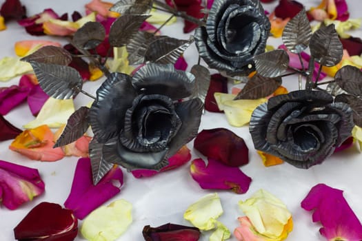 Metal roses made of steel against background of multicolored petals of living roses for the holiday