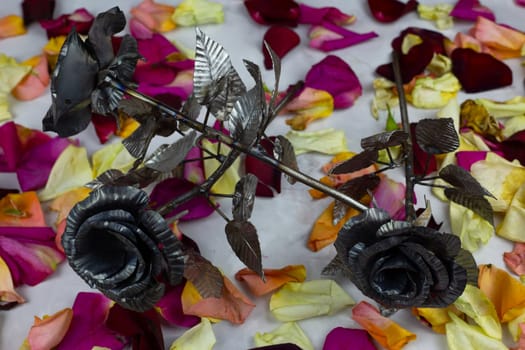 Metal roses as holiday gift, artificial flowers against the background of real rose petals