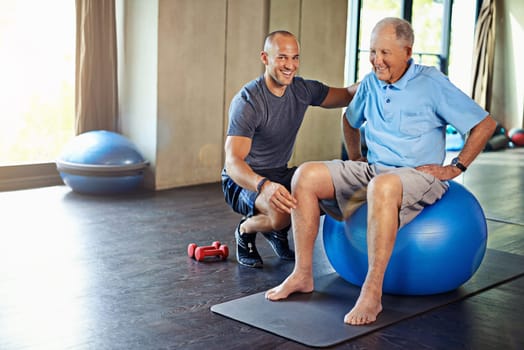 Physiotherapist, helping and senior man with yoga ball, training and elderly support for care. Men, gym and exercise for health, wellness and coaching with dumbbell for mature rehab and wellbeing.
