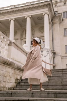 woman in elegant coat and hat against an intricate architectural backdrop, harmoniously blending modern fashion with historical allure. The soft daylight adds to its timeless appeal