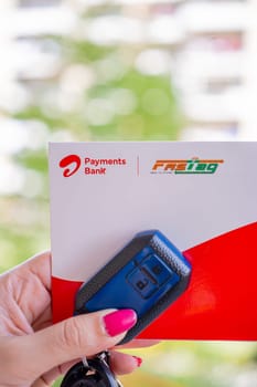 Delhi, India - 27th Mar 2024: Woman holding Airtel Payment bank Fastag with car key showing the new payment method from NHAI national highway authority of India for Toll