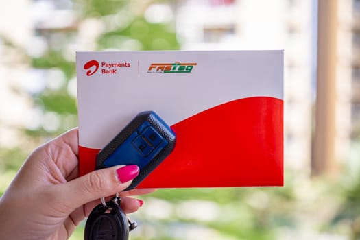 Delhi, India - 27th Mar 2024: Woman holding Airtel Payment bank Fastag with car key showing the new payment method from NHAI national highway authority of India for Toll