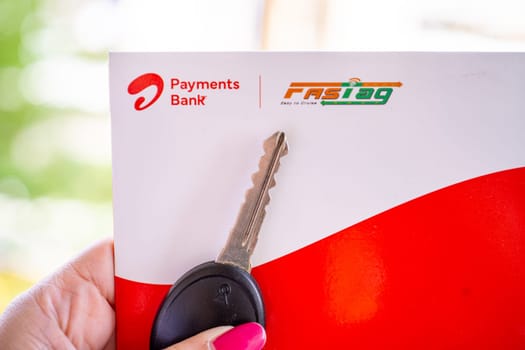 Delhi, India - 27th Mar 2024: Woman holding Airtel Payment bank Fastag with car key showing the new payment method from NHAI national highway authority of India for Toll