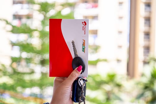 Delhi, India - 27th Mar 2024: Woman holding Airtel Payment bank Fastag with car key showing the new payment method from NHAI national highway authority of India for Toll