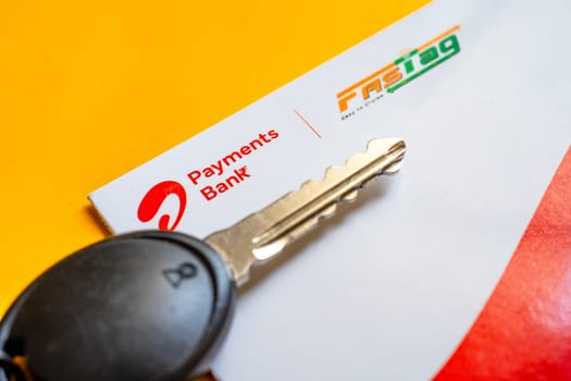 Delhi, India - 27th Mar 2024: Close up shot of Airtel Payment bank Fastag and car key placed on yellow table showing the RFID payment by NHAI