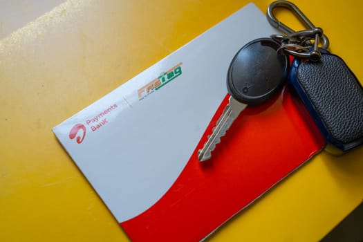 Delhi, India - 27th Mar 2024: Close up shot of Airtel Payment bank Fastag and car key placed on yellow table showing the RFID payment by NHAI