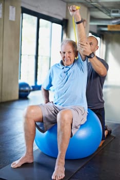 Physiotherapist, helping and senior man with elastic, training and elderly support for care. Men, gym and exercise for health, wellness and coaching with yoga ball for mature rehab and wellbeing.