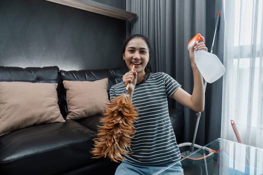 Asian woman happily use feather pick as microphone while cleaning house on the weekend.