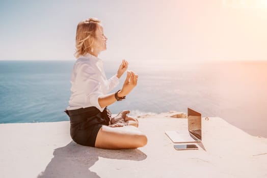 Happy girl doing yoga with laptop working at the beach. beautiful and calm business woman sitting with a laptop in a summer cafe in the lotus position meditating and relaxing. freelance girl remote work beach paradise