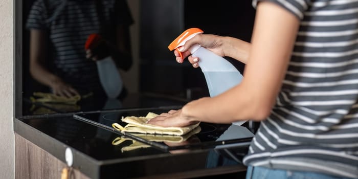 Asian woman cleaning the table surface with towel and spray detergent.