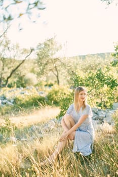 Girl sits on the stones in the park, hugging her raised knee and looking to the side. High quality photo