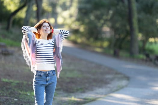 A woman wearing a striped shirt and jeans is walking down a path. She is smiling and looking up at the sky