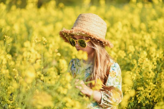 Girl in a dress and hat in a field of rapeseed smelling flowers