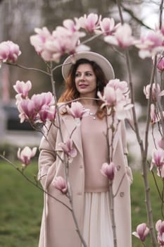 Woman magnolia flowers, surrounded by blossoming trees, hair down, white hat, wearing a light coat. Captured during spring, showcasing natural beauty and seasonal change