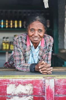 Ranohira, Madagascar - April 29, 2019: Unknown Malagasy woman shopkeeper leaning at table, smiling, in her market stall on the street. People of Madagascar are poor but cheerful