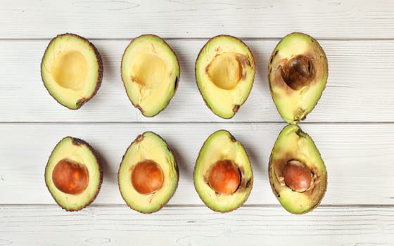 Avocado halves sorted from ripe to overripe on white boards desk, view from above