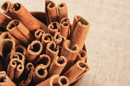 Closeup detail - Heap of cinnamon bark sticks in wooden cup on linen tablecloth. 