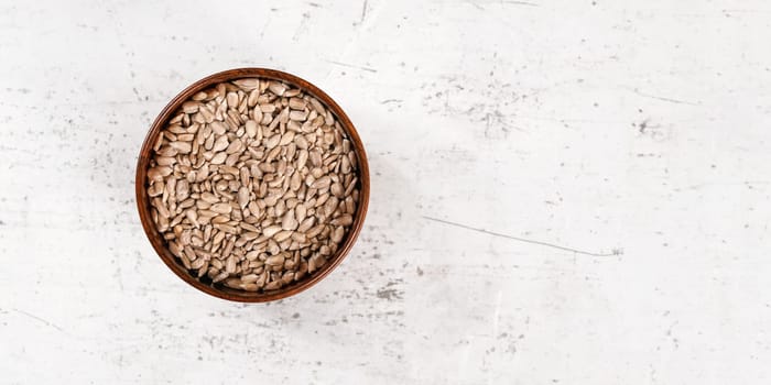 Sunflower seeds in small wooden bowl laying on white stone board, view from above, wide photo with empty space for text right side