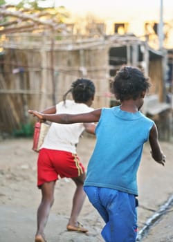Two African kids playing, running on dusty road, view from behind