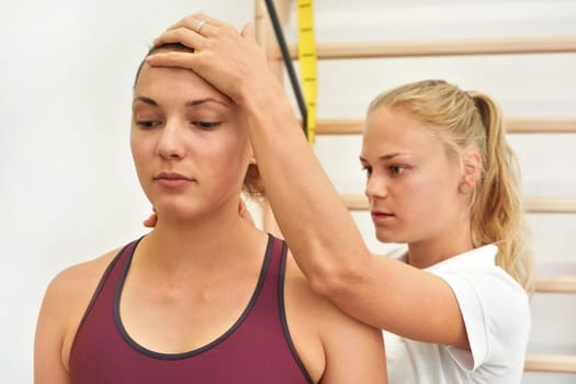 Young physiotherapist exercising with her female patient, fixing head and neck using hand, during exercise