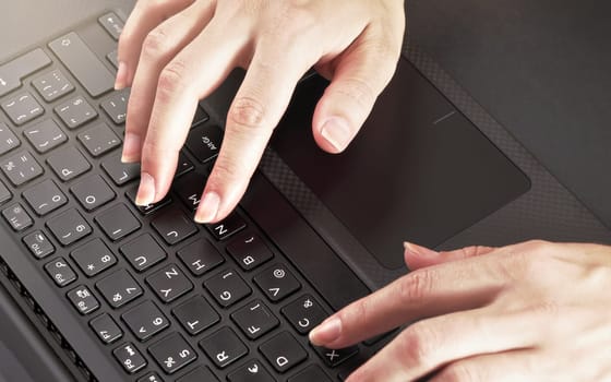 Woman hands typing on black laptop keyboard, close up detail from above