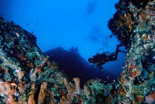 Scuba diver underwater portrait in the deep blue ocean and backlight sun and giant red sponge at liberty wreck in bali indonesia