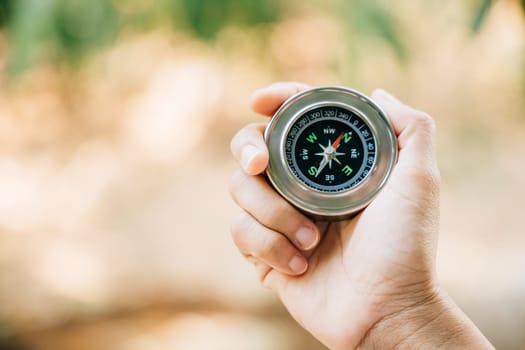 In the forest a hiker conquers confusion by holding a compass. The traveler hand with the compass signifies guidance and a journey filled with exploration and discovery.