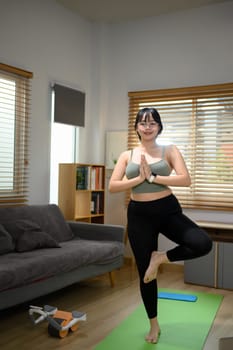 Full length young woman practicing yoga on mat in living room. Healthy lifestyle concept.