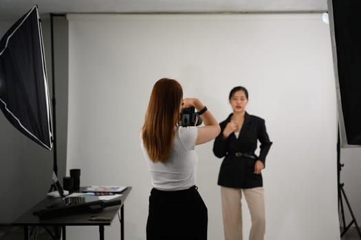 Fashion photographer taking picture of female model with digital camera in lighting studio.