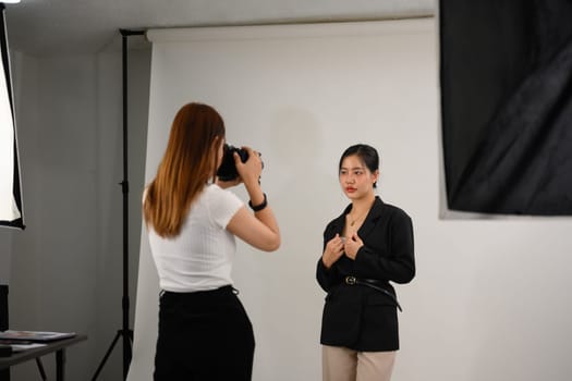 Fashion photographer taking picture of female model with digital camera in lighting studio.