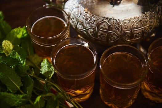 Close up view of glasses with green tea with mint and silver teapot near fresh mint leaves. Moroccan traditional tea. Beverage. Refreshing drink. National beverage in Morocco