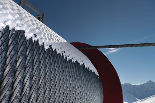 A large reel of steel cable covered with snow against the backdrop of mountains. Construction of a cable car in the mountains.