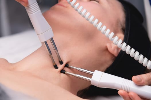 Close-up of a woman receiving an electric neck massage with equipment in a beauty salon. Used for therapy with a multifunctional electro massage device.