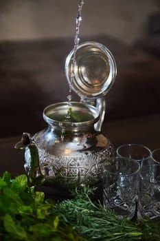 Pouring boiling water into a silver teapot while preparing traditional Moroccan mint tea. A tea break during Aid El Fitr or Ramadan. The a la menthe as symbol of Moroccan hospitality