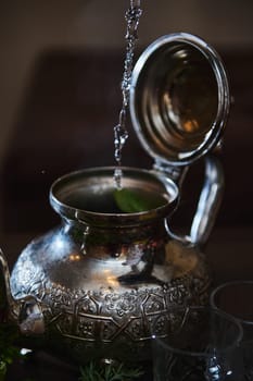 Pouring boiling water into a silver teapot while preparing traditional Moroccan mint tea. A tea break during Aid El Fitr or Ramadan.