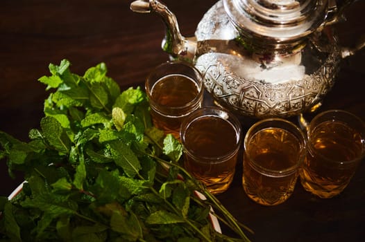 View from above Drinking glasses with fresh Moroccan tea with mint and silver traditional tea pot on wooden table. Enjoy a tea break in Moroccan traditions during Ftour Ftor at Ramadan or Aid Al Fitr