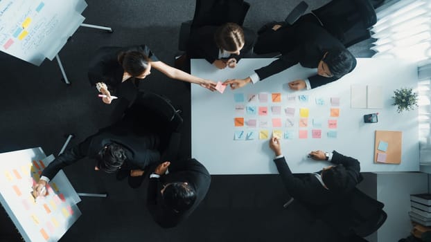 Top down aerial view of business group sharing and brainstorming idea by using sticky notes at meeting room. Investor writing marketing strategy on board while receive note from manager. Directorate.
