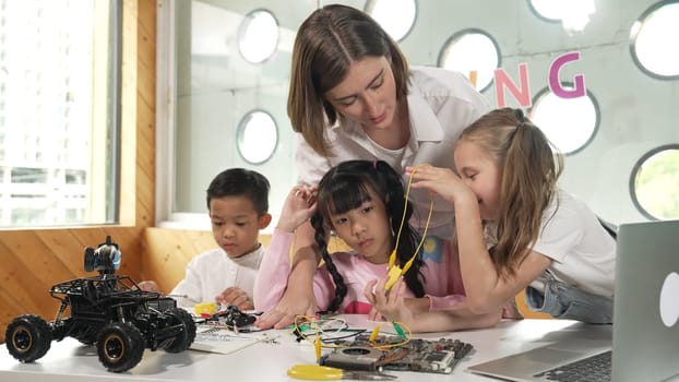 Teacher looking at children while diverse student looking at screen. Children excited in presentation while drawing or writing art books at table with toys and color pencil placed on table. Erudition.