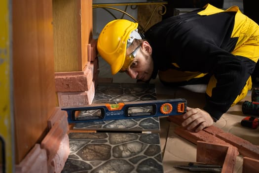 While laying the terracotta, the general construction worker checks the correctness of execution with a spirit level. An employee wearing personal protective equipment.