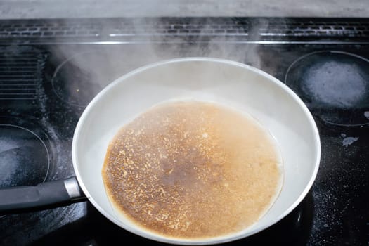 A large frying pan stands on the induction cooker and inside it is a pancake dough that is fried. The water evaporates from the pan.