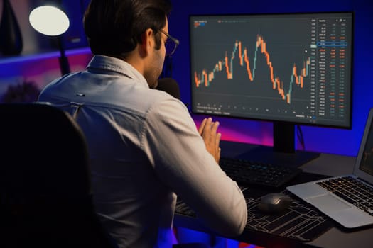 Smart trader businessman concentrating on dynamic stock exchange investment on pc and laptop showing on screen with high profit in searching market at neon light office in dark room night. Surmise.