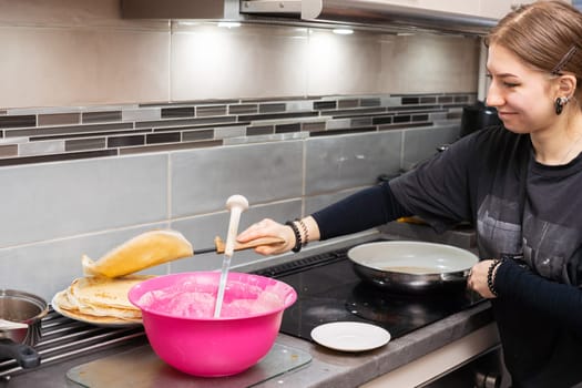 A young home cook carries a fried pancake onto a plate. Tasty homemade pancakes from a young woman's hand.