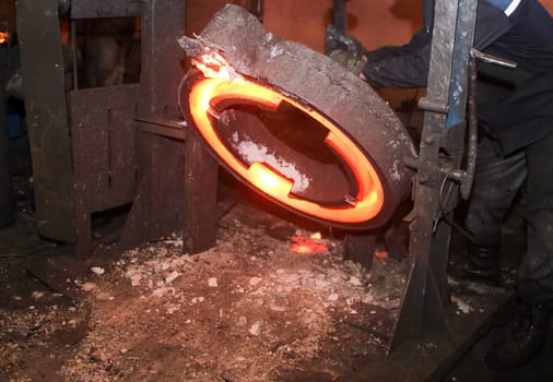 An industrial forging press machine shaping glowing hot metal disk with sparks. Made of cast iron, powered by a motor, hammering metal with a large hammer, shaped to desired shape.