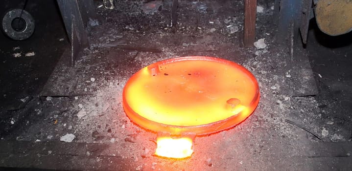 Industrial metalworking or manufacturing concept. Glowing hot round metal disc forging press isolated on black background. Industrial concept of power, energy, and strength.