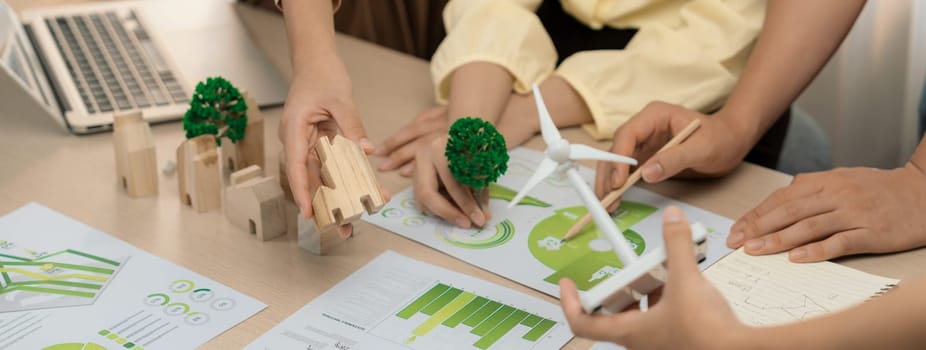 Windmill model represented using renewable energy placed during presenting green business on table with wooden block and environmental document scatter around. Closeup. Delineation.