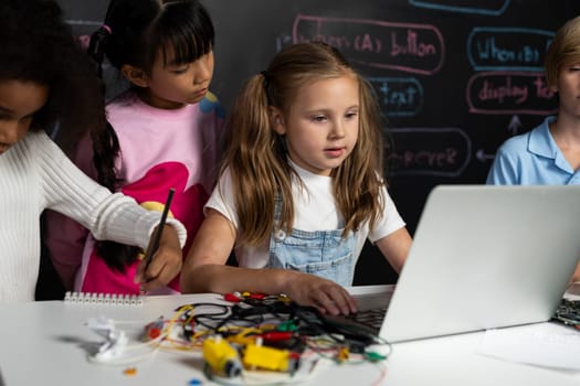 Smart girl in white bib learning about coding robotics technology using laptop in the STEM class. Schoolboy in blue shirt try to educate motherboard while smart schoolgirls reading code. Erudition.