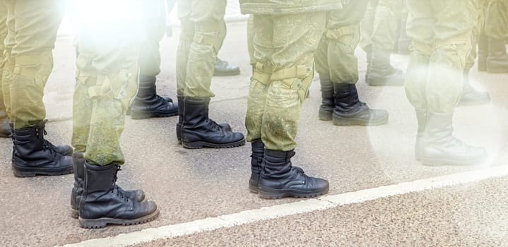Army soldiers in uniform stand in formation on a concrete surface with yellow crosswalk lines. They wear combat fatigues and boots, showing discipline and readiness.