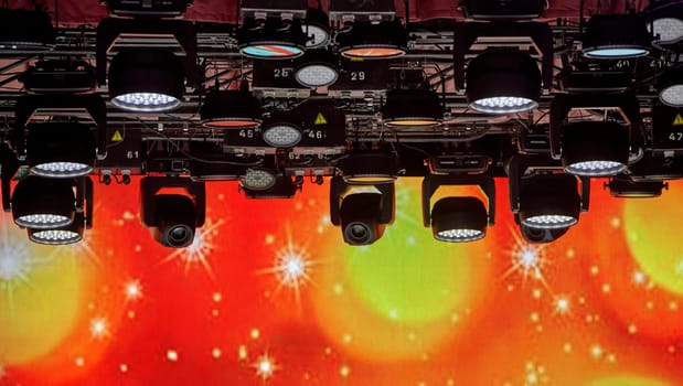 A lot of spotlights on the ceiling of the concert hall. Bright stage lights are on. The spotlights are arranged in a grid pattern. The stage is dark. The spotlights are creating a dramatic effect.
